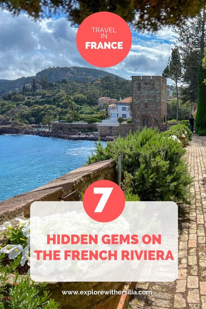 A Pinterest-style travel pin featuring a coastal scene from the French Riviera with a medieval stone tower along a seaside path, turquoise Mediterranean waters, and lush hillside villas. The image includes coral-colored text overlays reading 'TRAVEL IN FRANCE' and '7 HIDDEN GEMS ON THE FRENCH RIVIERA'.