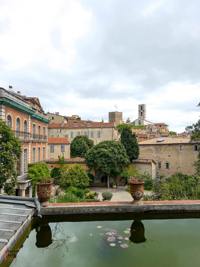 View from Fragonard perfume factory's garden terrace in Grasse, showing a lily pond in the foreground and the medieval town rising up the hill behind, with its characteristic church tower and historic buildings with terracotta roofs