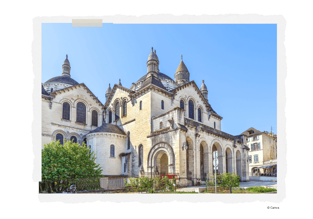 Exterior view of Saint-Front Cathedral in Périgueux featuring its distinctive Byzantine-inspired architecture with multiple domes, cream-colored limestone façade, Romanesque arches, and decorative elements against a bright blue sky, with small gardens and iron fencing in the foreground.