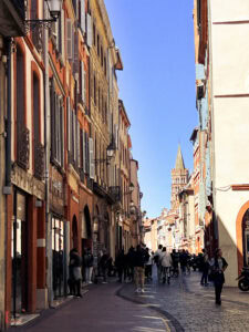 Narrow street in Toulouse's historic center with Saint-Sernin tower visible in distance