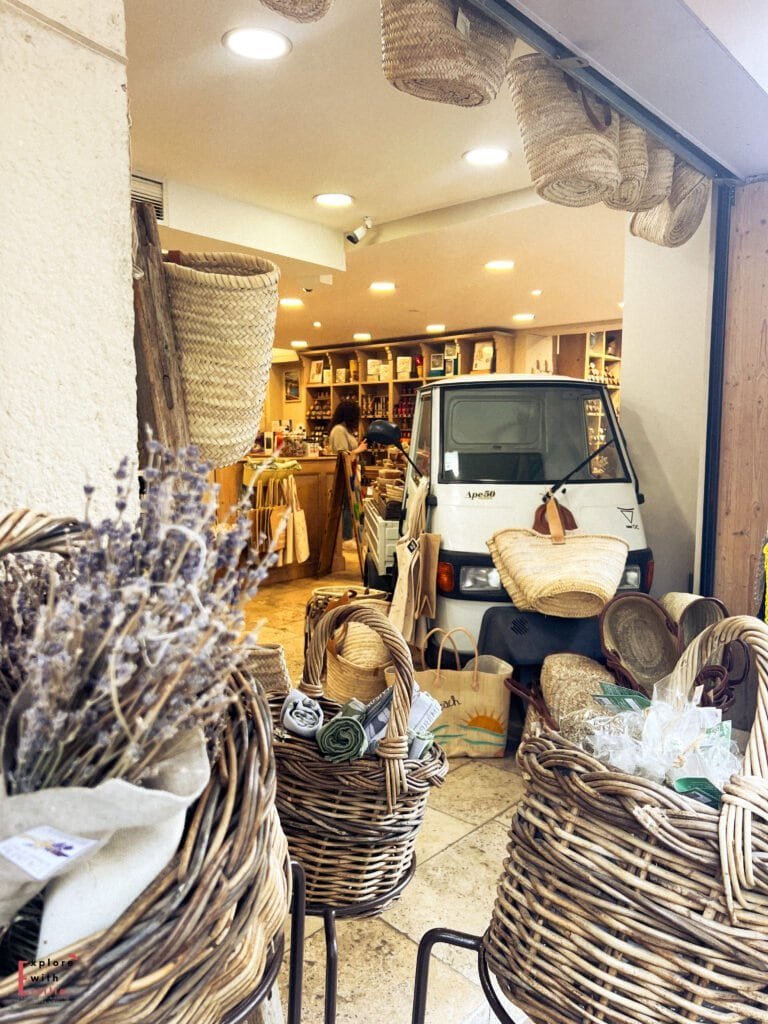 A charming Provençal shop in Avignon, France, filled with woven baskets, lavender bundles, and local goods. A small white delivery vehicle is parked inside, surrounded by rustic decor and artisanal products, creating an inviting, authentic market atmosphere.