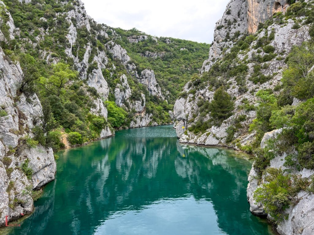Stunning view of the Gorges du Verdon in Provence, featuring turquoise-green river water winding between steep limestone cliffs covered in dense greenery. The tranquil scene reflects the natural beauty and dramatic landscapes of one of Europe’s most spectacular river canyons.