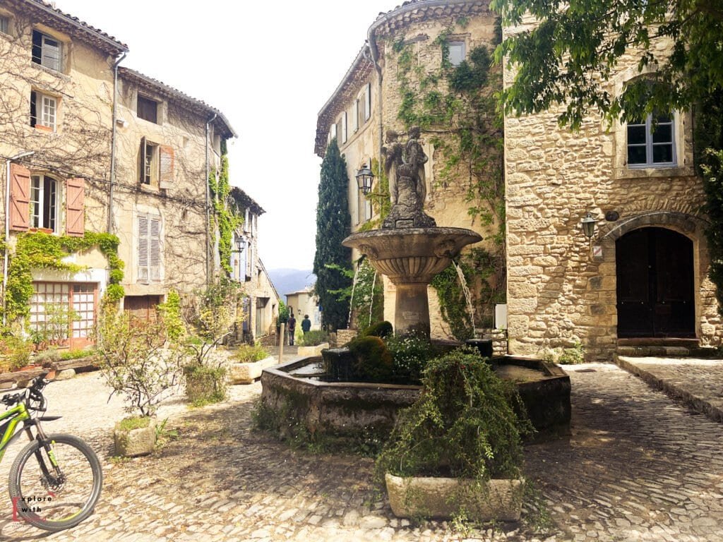 Peaceful square in Saignon, one of the best villages to see in Provence, featuring a moss-covered fountain, cobbled streets, and ivy-draped stone buildings—perfect for a quiet escape on a day trip from Aix en Provence.