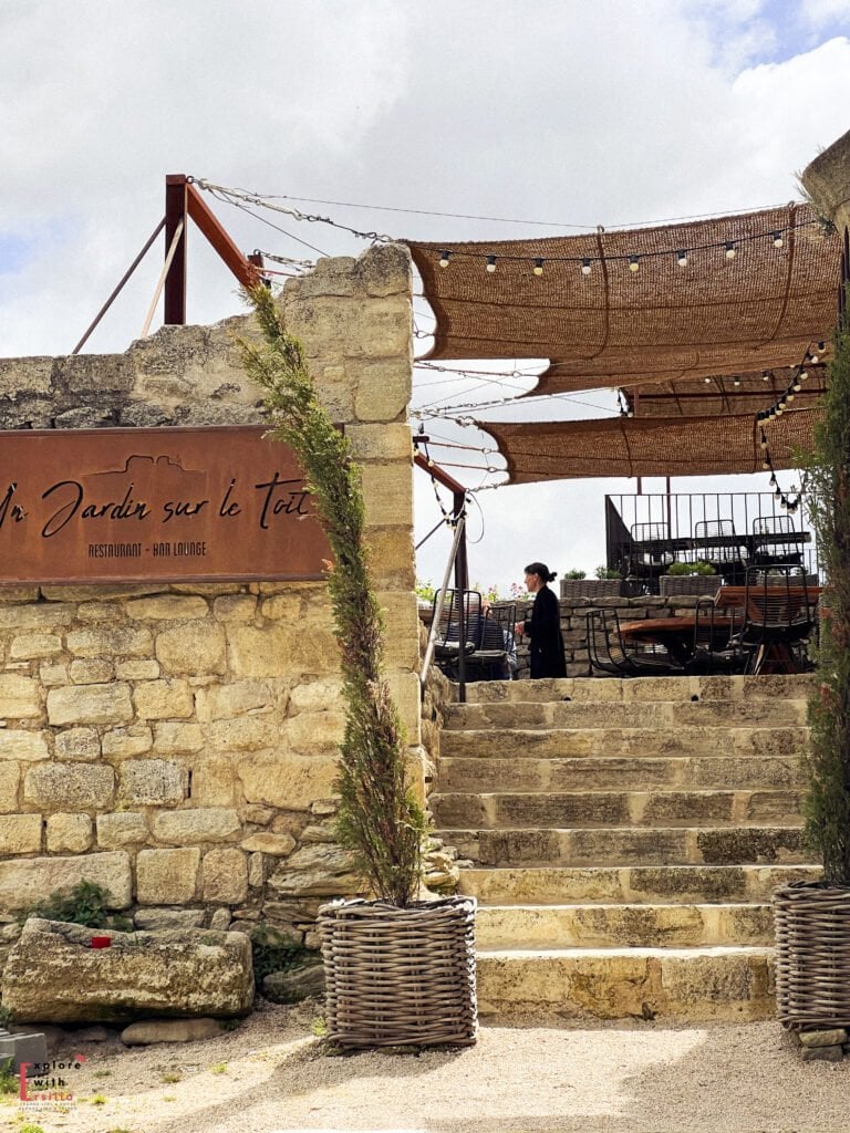 Stone stairway leading up to “Un Jardin sur le Toit” restaurant and bar lounge in Saignon village, a hidden gem in Provence. The rustic terrace features woven shade canopies and charming decor, blending perfectly with the historic stone architecture.